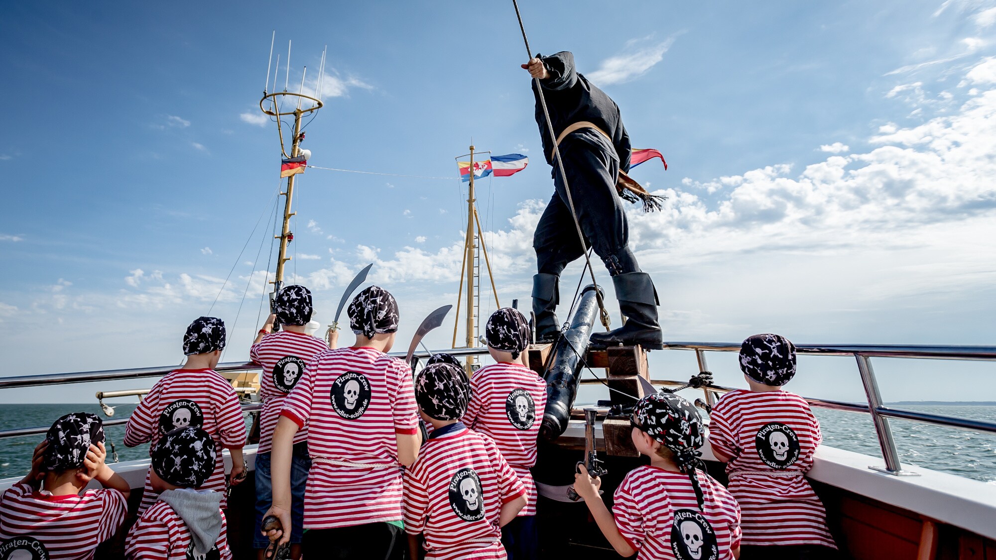 Ein verkleideter Pirat mit Kindern am Bug eines Schiffes auf dem Meer