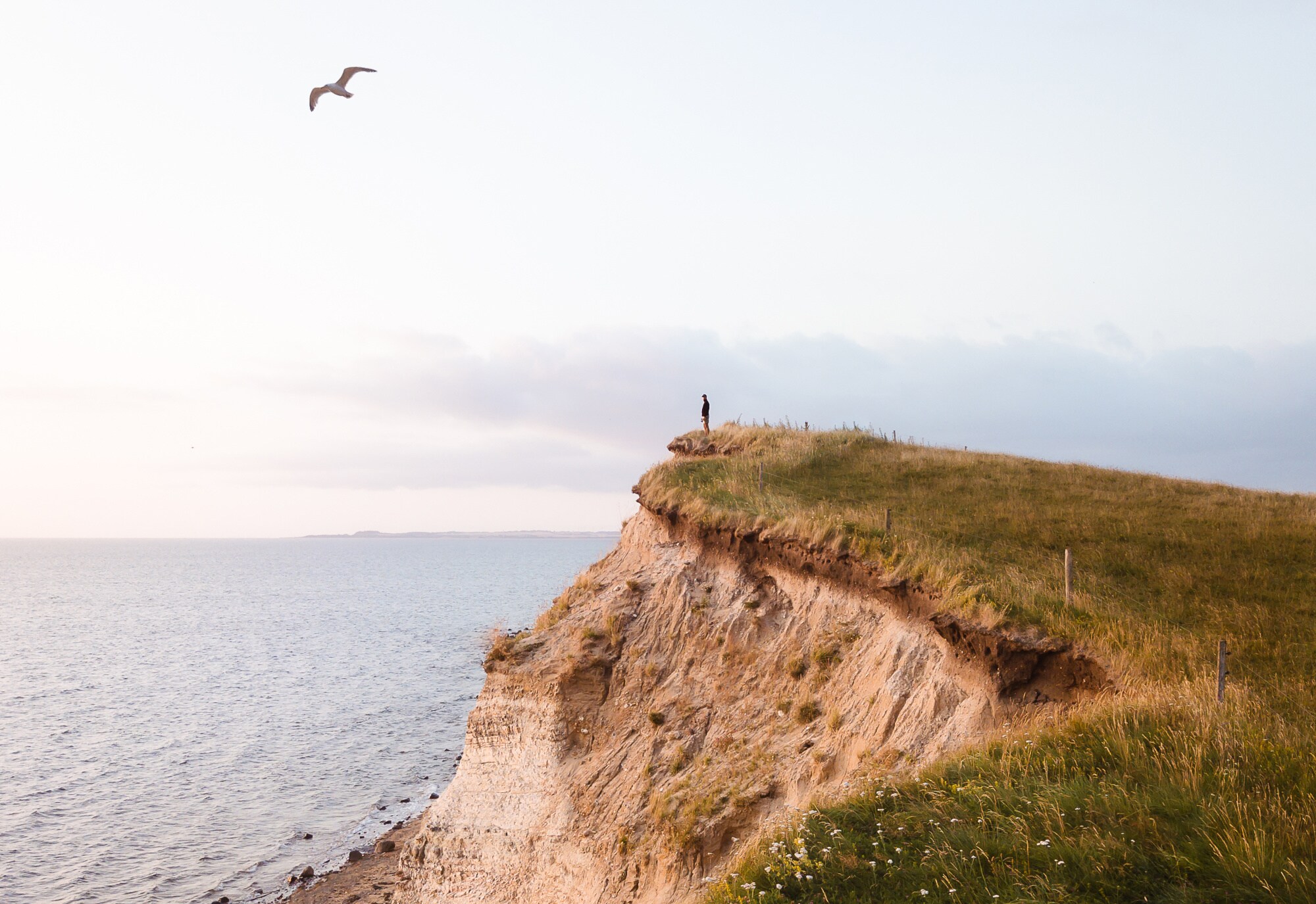 Eine Person steht auf einer Klippe und blickt aufs Meer