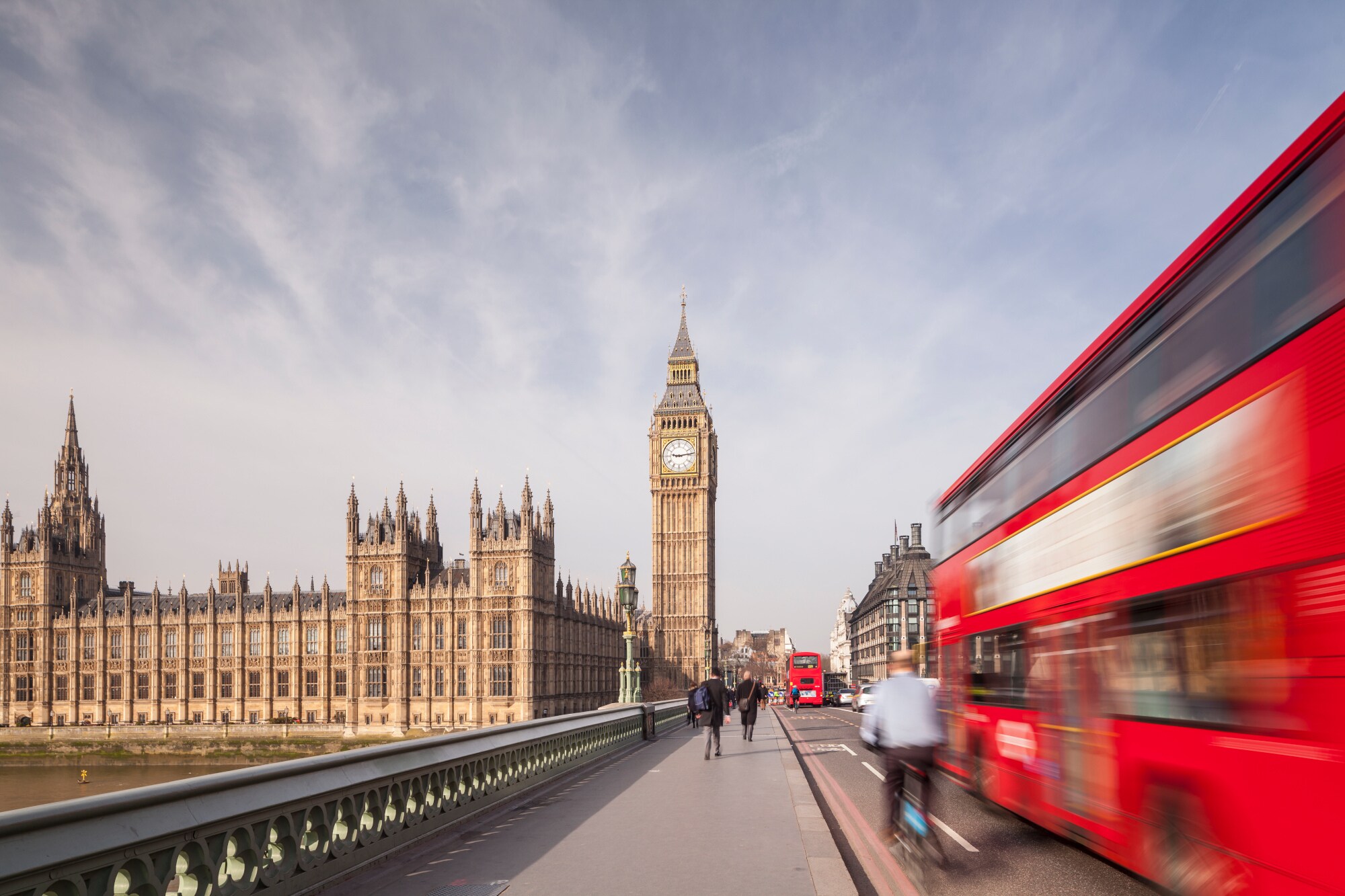 Big Ben und Houses of Parliament am Ende einer Brücke, auf der rote Doppeldeckerbusse fahren