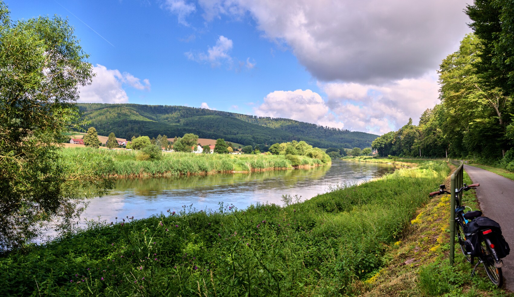 Panorama vom Fernradweg an der Weser im Weserbergland mit grünen Ufern und leicht bewölktem Himmel Panorama vom Fernradweg an der Weser im Weserbergland mit grünen Ufern und leicht bewölktem Himmel