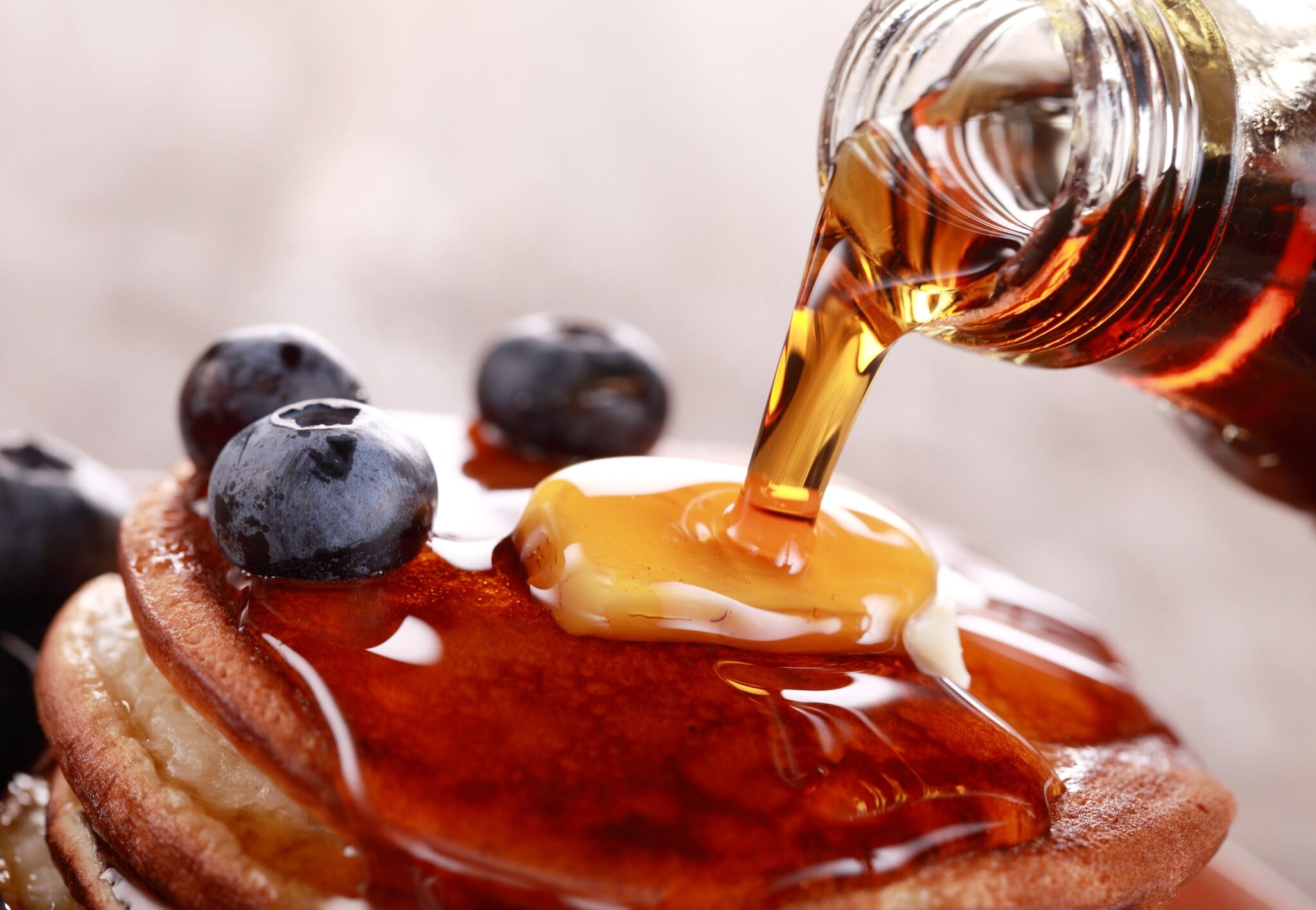 Über einen Stapel Pancakes mit Heidelbeeren und Bananenscheibe fließt Ahornsirup. Über einen Stapel Pancakes mit Heidelbeeren und Bananenscheibe fließt Ahornsirup.