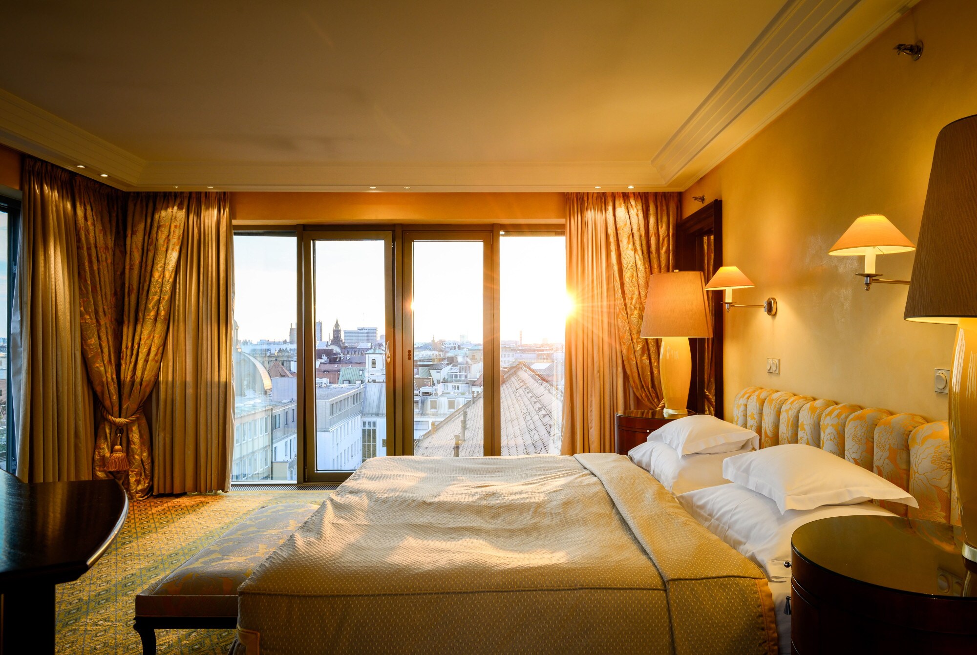 Elegante Hotelsuite mit goldenen Textilien und bodentiefen Fenstern mit Blick auf die Münchner Innenstadt Elegante Hotelsuite mit goldenen Textilien und bodentiefen Fenstern mit Blick auf die Münchner Innenstadt