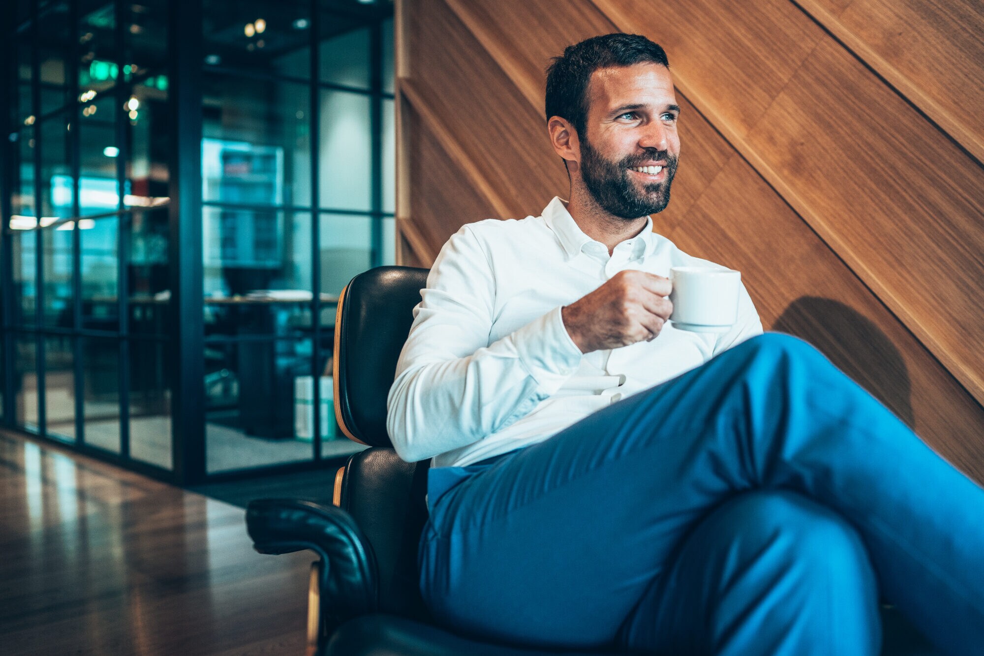 Ein Geschäftsmann sitzt entspannt mit einer Kaffeetasse in einem Sessel in einer Flughafen-Lounge Ein Geschäftsmann sitzt entspannt mit einer Kaffeetasse in einem Sessel in einer Flughafen-Lounge