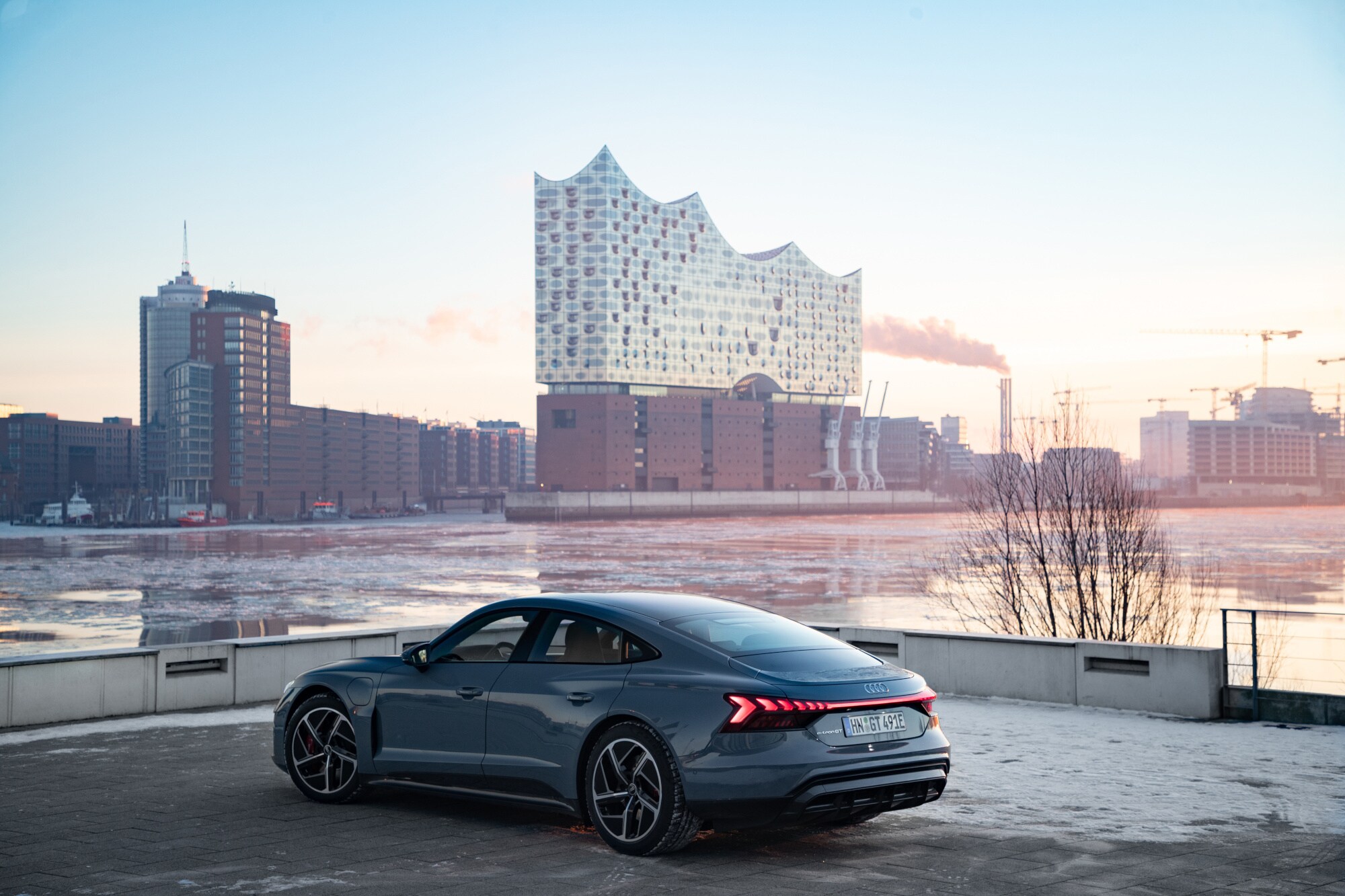 Ein AUDI e-tron GT an der Elbe in Hamburg, im Hintergrund die Elbphilharmonie