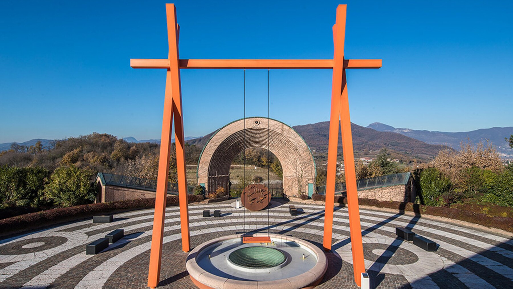 Eine Schaukel mit orangem Holzgerüst auf einer Plattform vor Bergkulisse