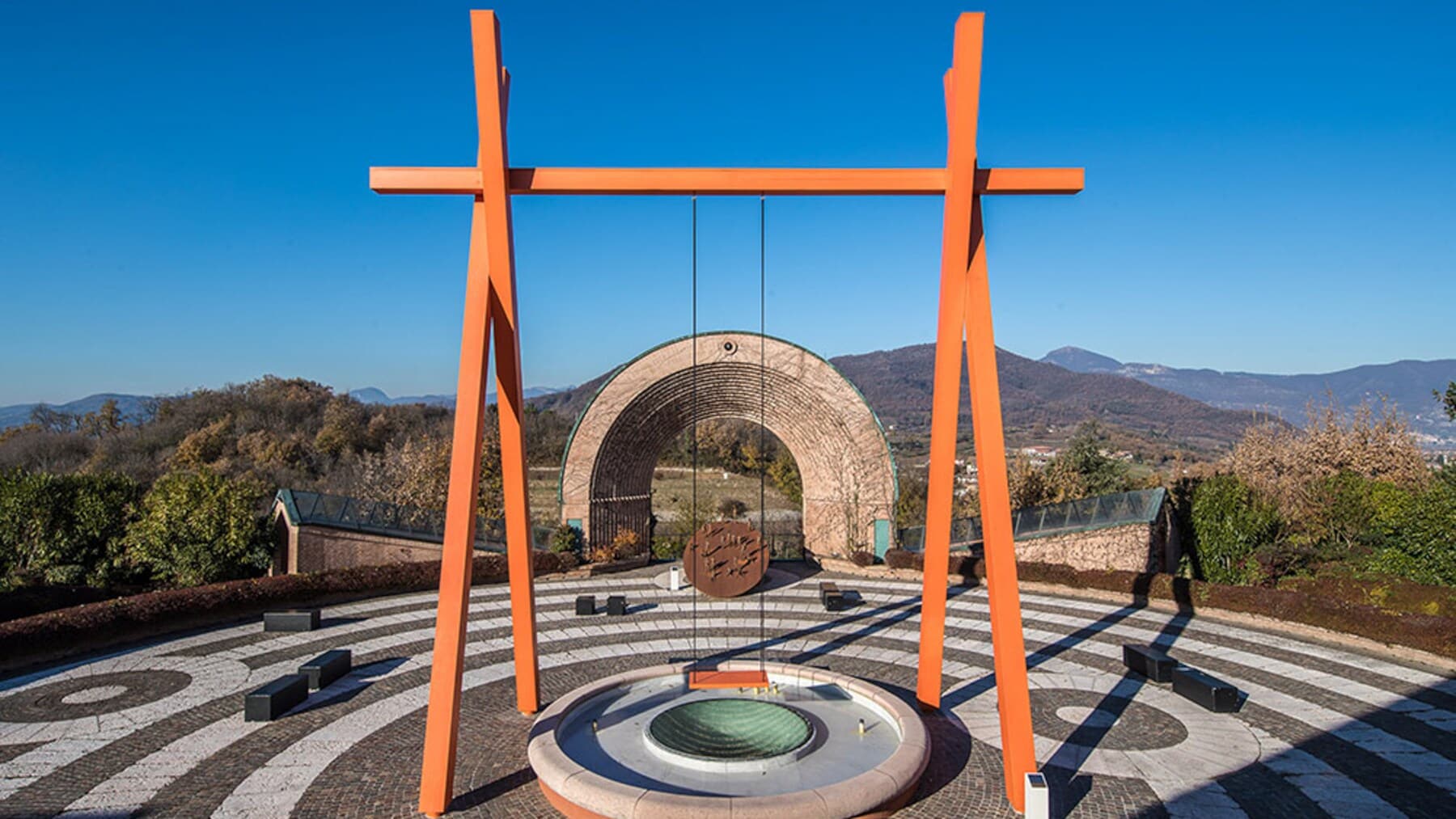 Eine Schaukel mit orangem Holzgerüst auf einer Plattform vor Bergkulisse Eine Schaukel mit orangem Holzgerüst auf einer Plattform vor Bergkulisse