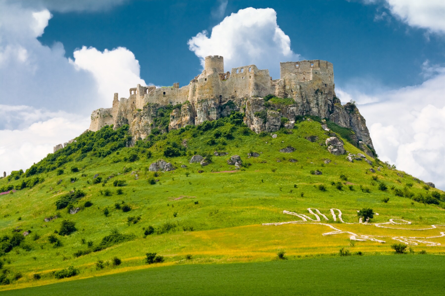 Eine Burganlage auf einem Berg, umringt von grünen Wiesen
