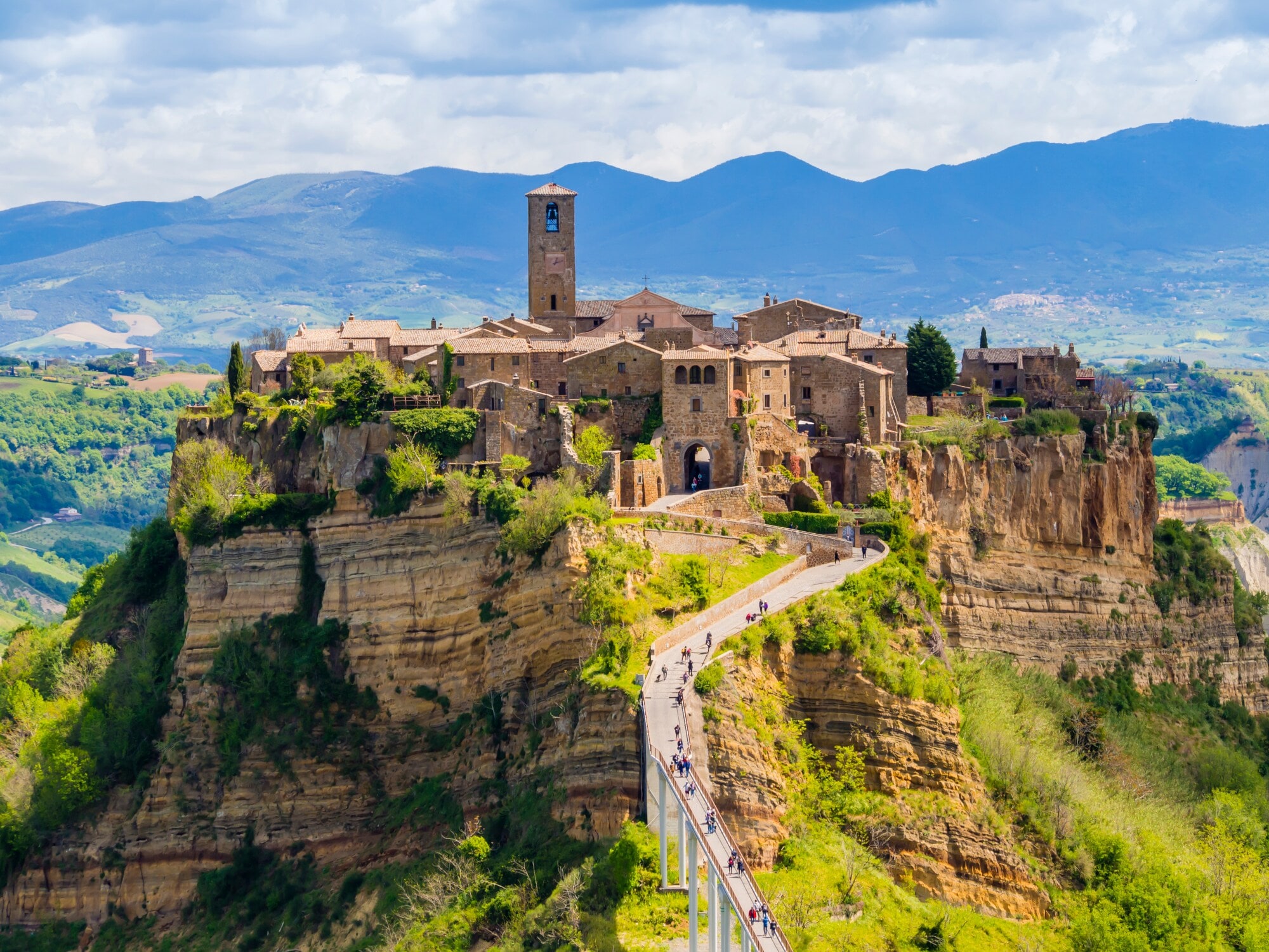 italien-regionen-civita-di-bagnoregio Ein mittelalterliches Dorf auf einem Tufffelsen mit Zugang über eine Fußgängerbrücke in einer grünen Hügellandschaft