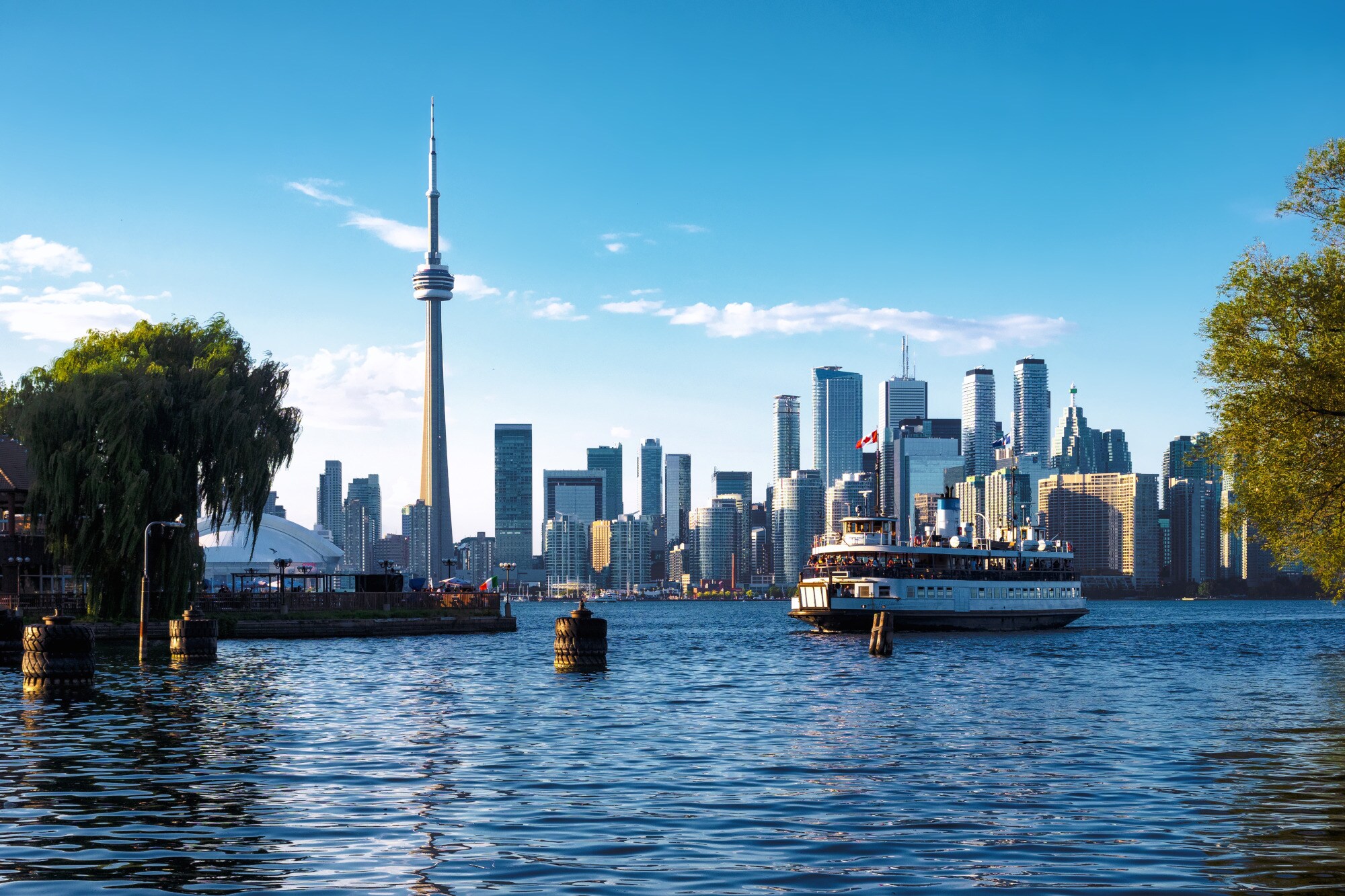 Blick auf die Skyline von Toronto mit dem bekannten CN Tower, im Vordergrund eine Fähre auf dem Wasser Blick auf die Skyline von Toronto mit dem bekannten CN Tower, im Vordergrund eine Fähre auf dem Wasser