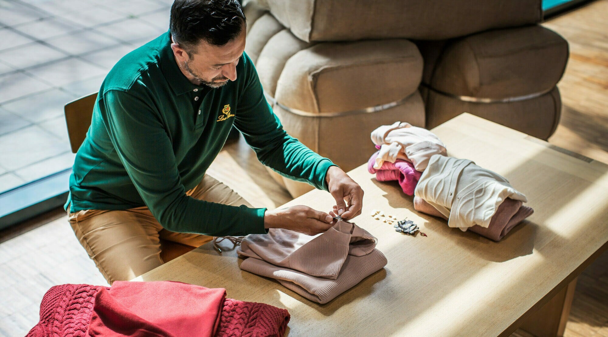 Mann sitzt an Tisch und näht Etikett in einen Pullover