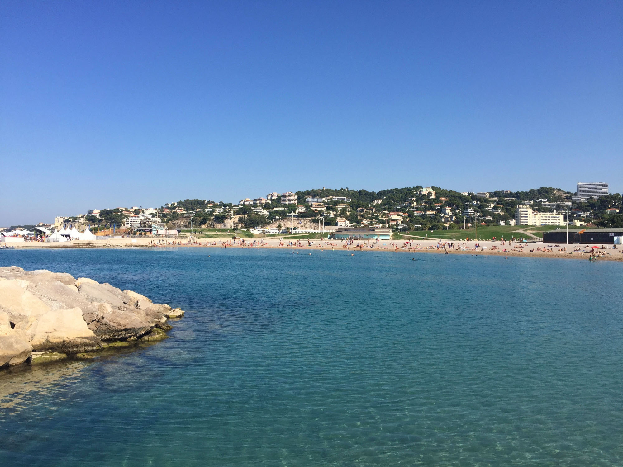 Meer im Vordergrund, weiter hinten Strand und eine hügelige Landschaft mit Häusern