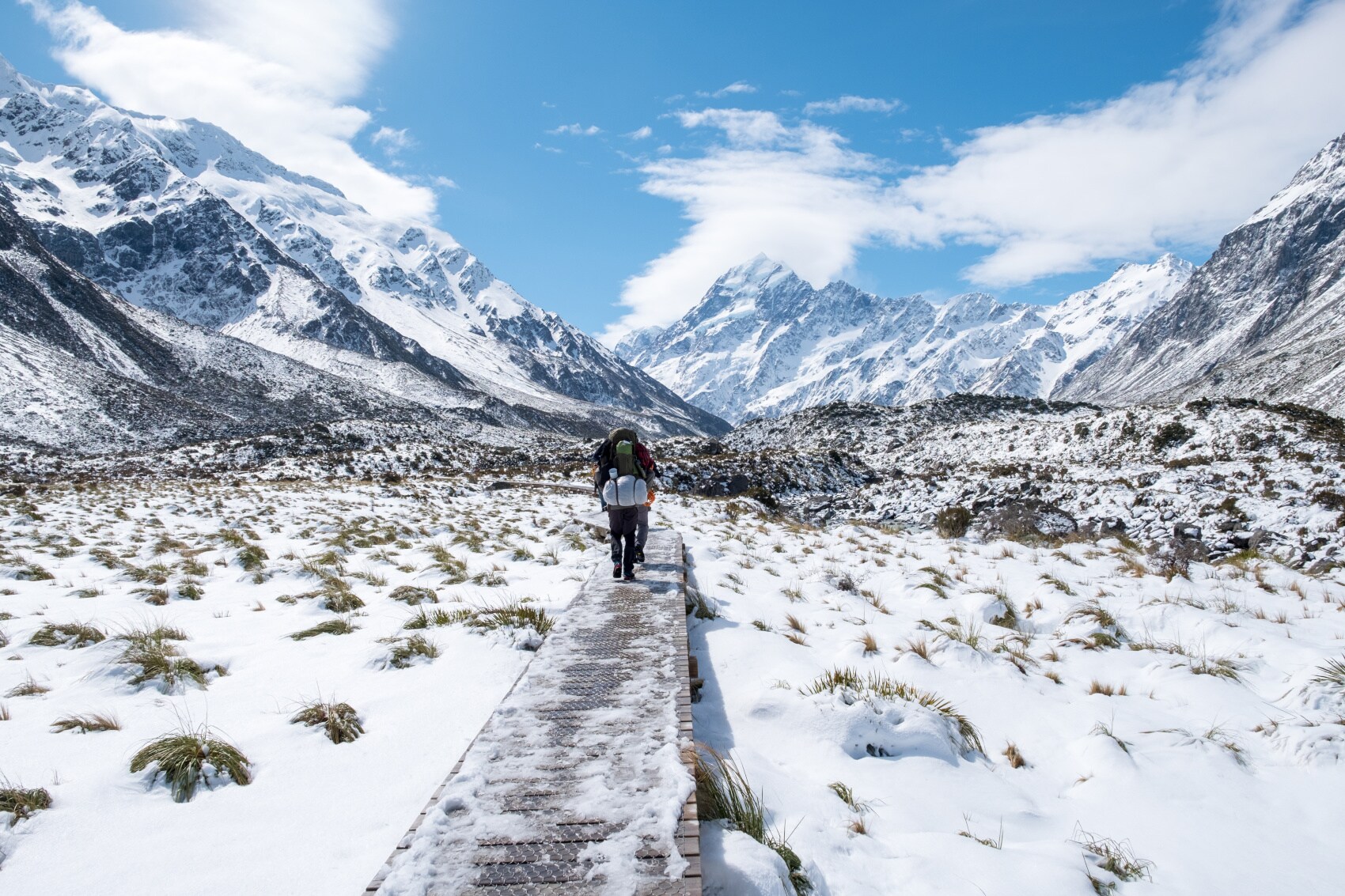 Eine Person in Wandermontur geht einen Weg zwischen schneebedeckten Bergen entlang Eine Person in Wandermontur geht einen Weg zwischen schneebedeckten Bergen entlang