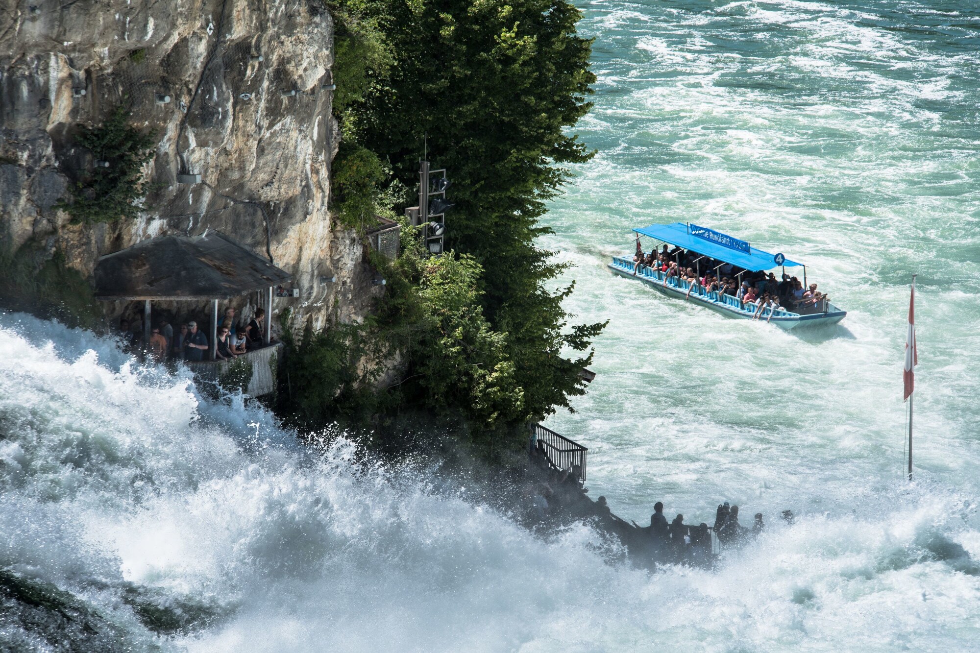 Personen in einem Ausflugsboot und Personen auf einer Aussichtsplattform an einem Wasserfall