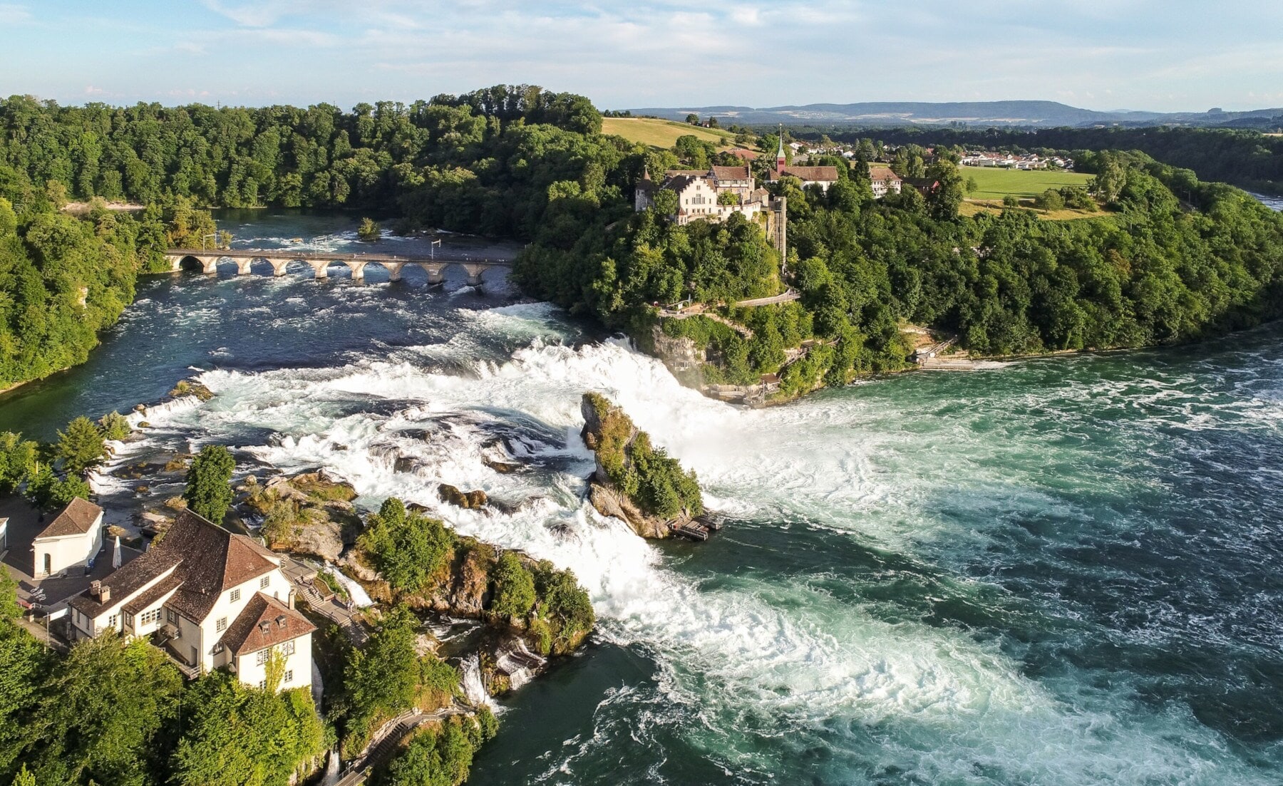 Luftaufnahme des Rheinfalls mit Schloss Laufen inmitten bewaldeter Natur Luftaufnahme des Rheinfalls mit Schloss Laufen inmitten bewaldeter Natur