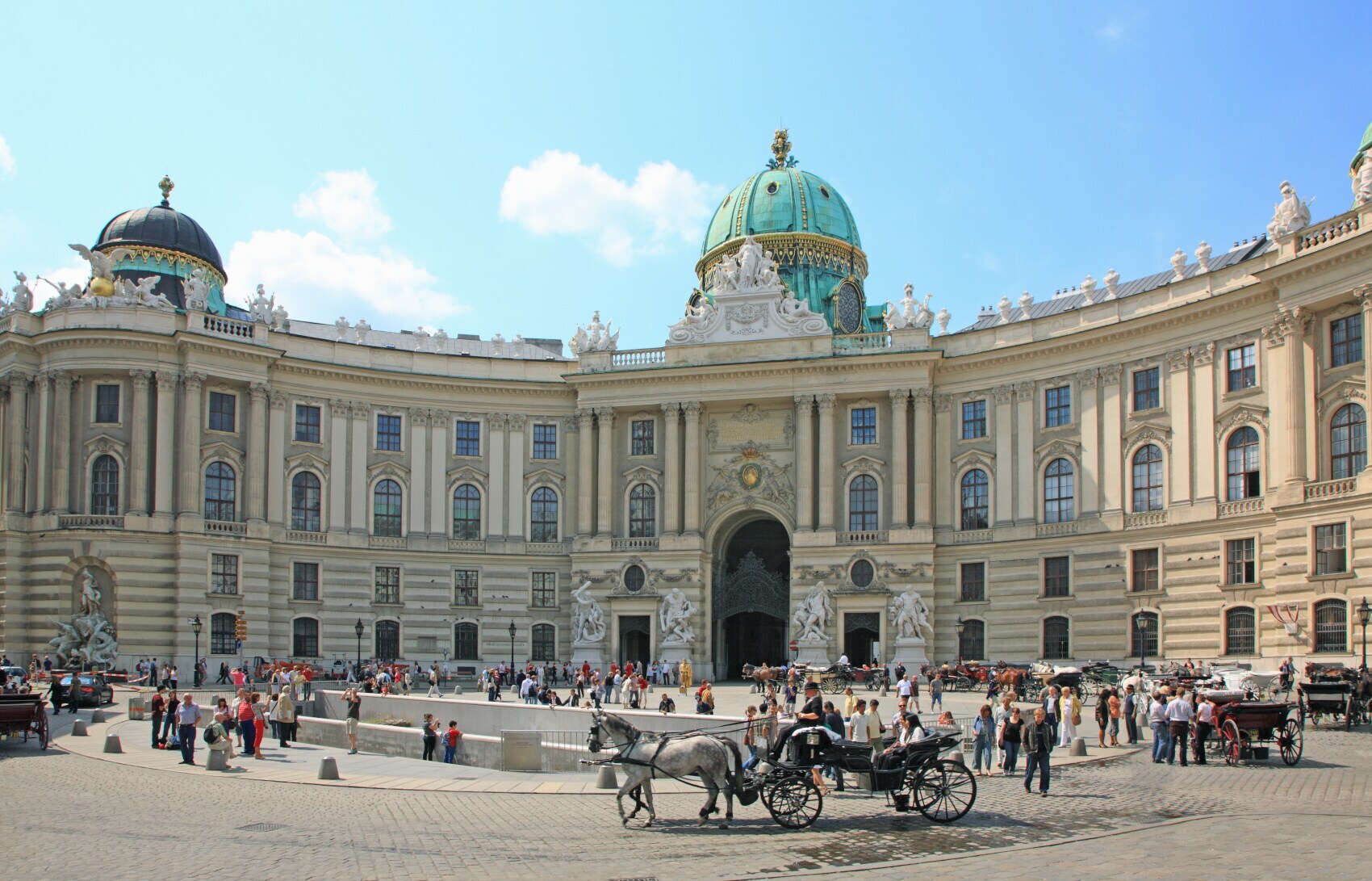 Personen und Pferdekutschen auf einem Platz vor der Wiener Hofburg