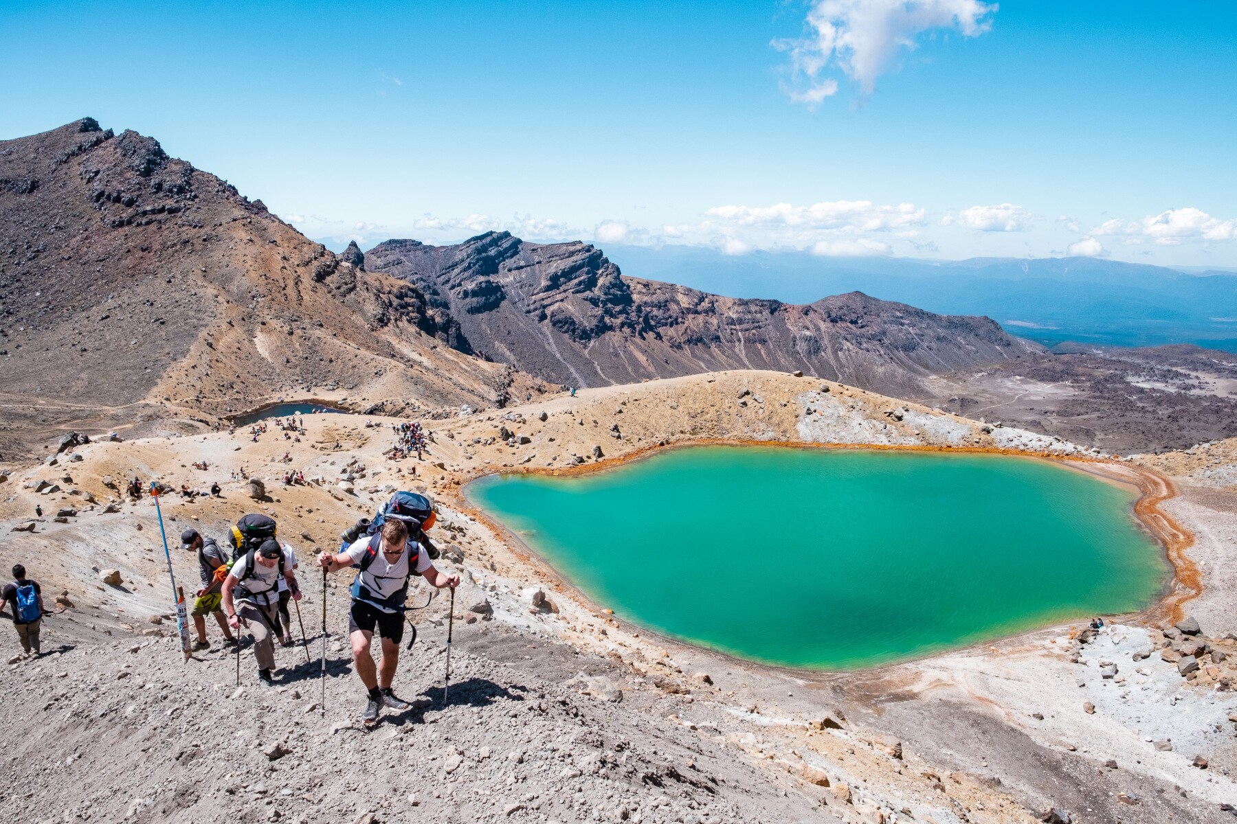 Mehrere wandernde Personen auf einem kargen Berg neben einem grün schimmernden Bergsee