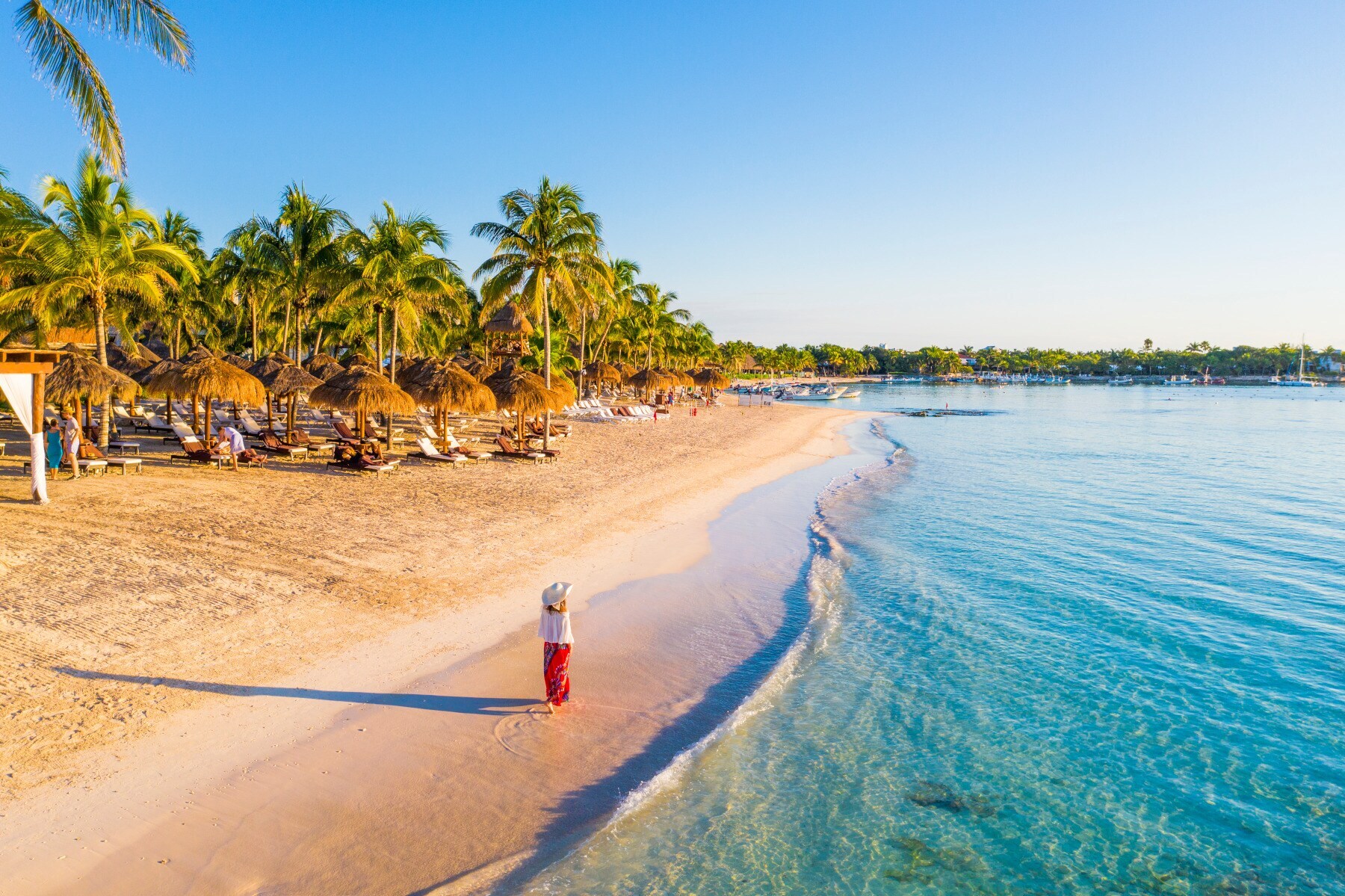 Eine Frau geht einen karibischen, palmengesäumten Sandstrand entlang