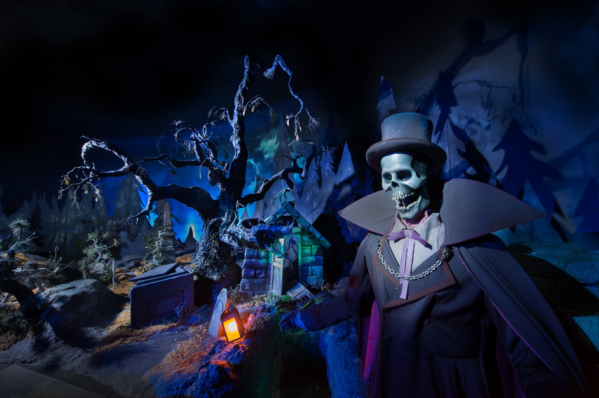 Ein angekleidetes, künstliches Skelett mit Zylinder in einer dunklen Landschaft im Inneren einer Geisterbahn