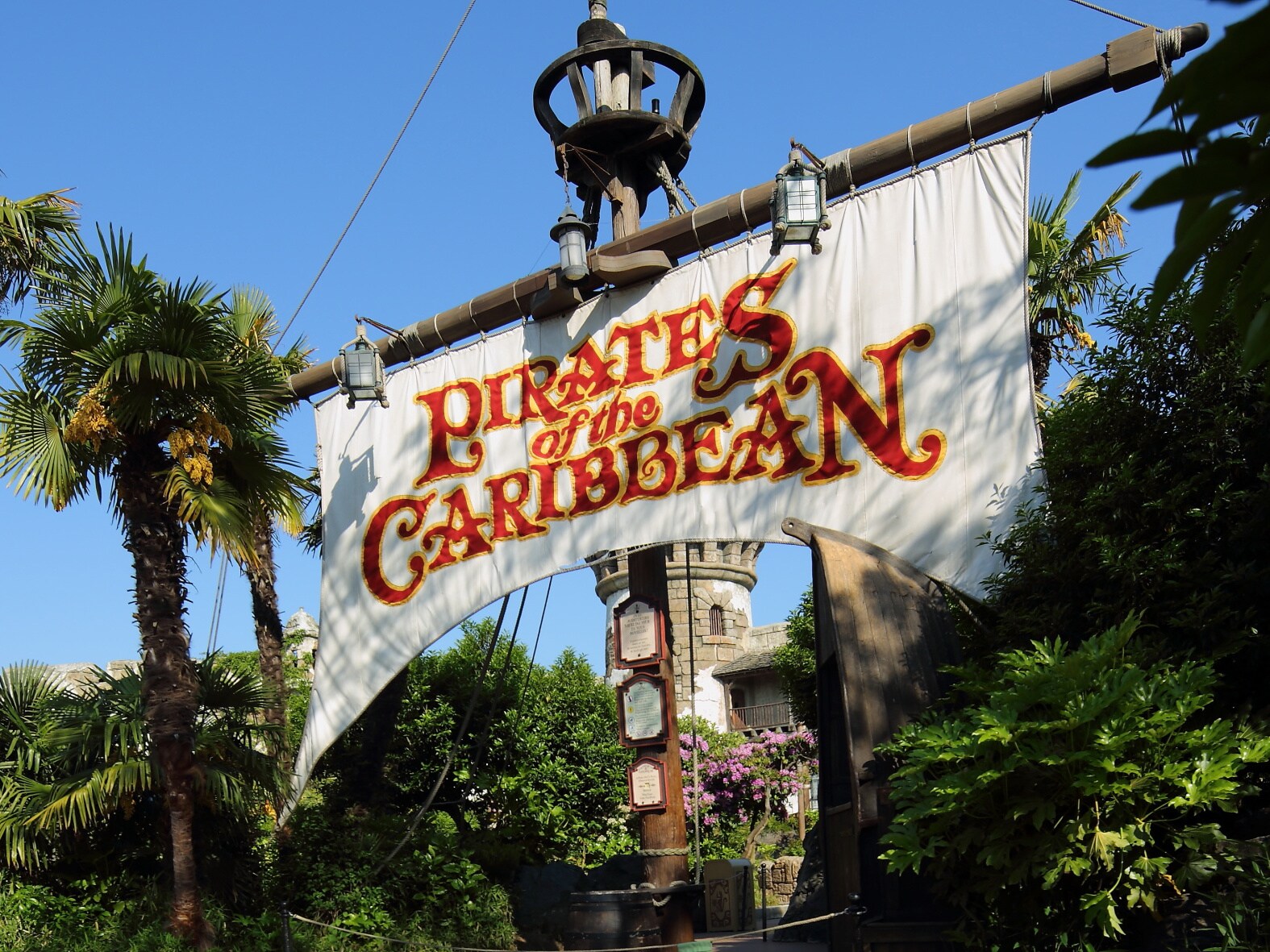 Ein weißes Segel mit der Aufschrift Pirates of the Caribbean an einem großen Schiffsmast am Eingang einer Attraktion in einem Themenpark