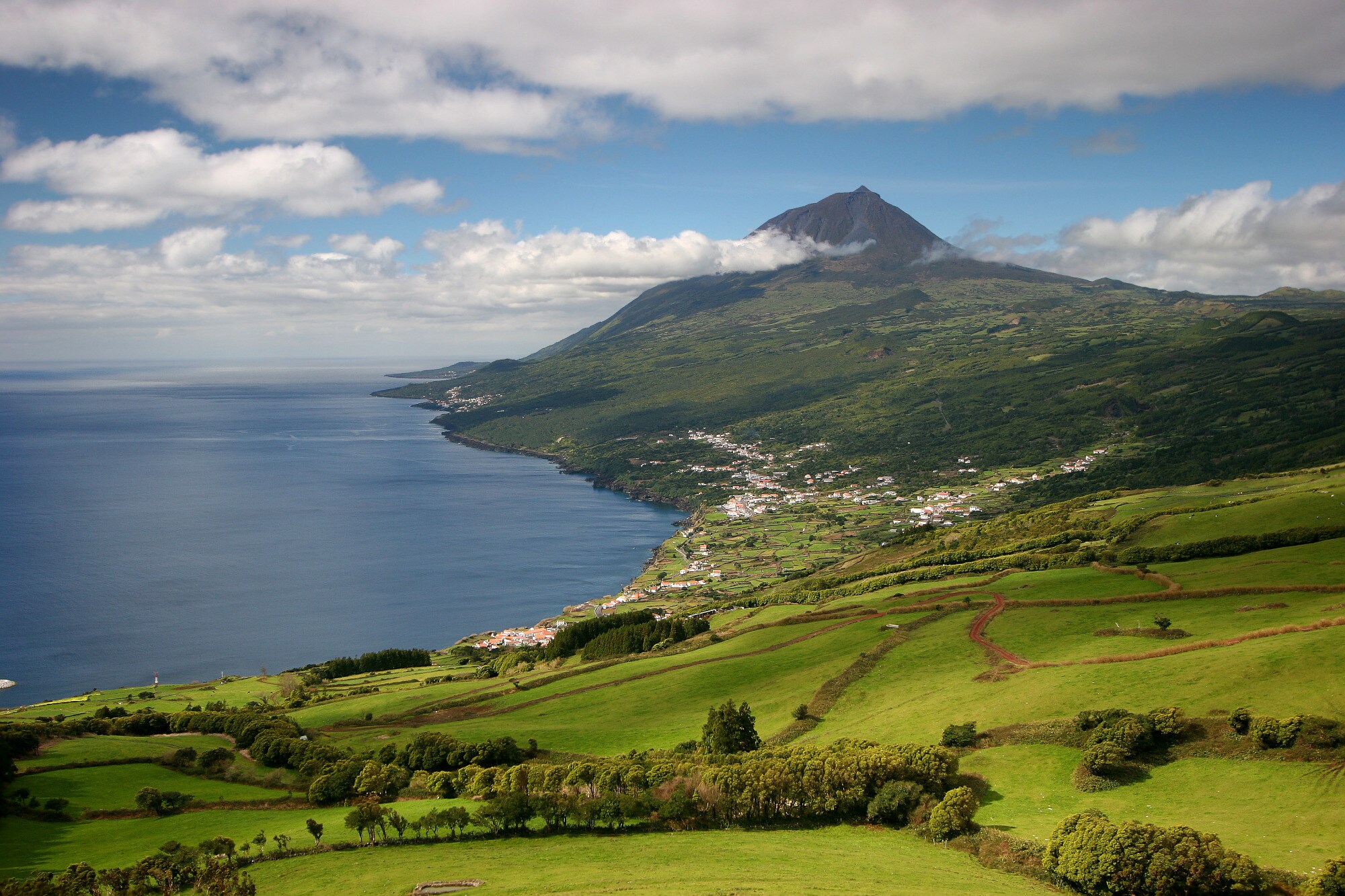 Ein Teil einer grün bewachsenen Insel am Meer mit einem hohen Berggipfel im Hintergrund