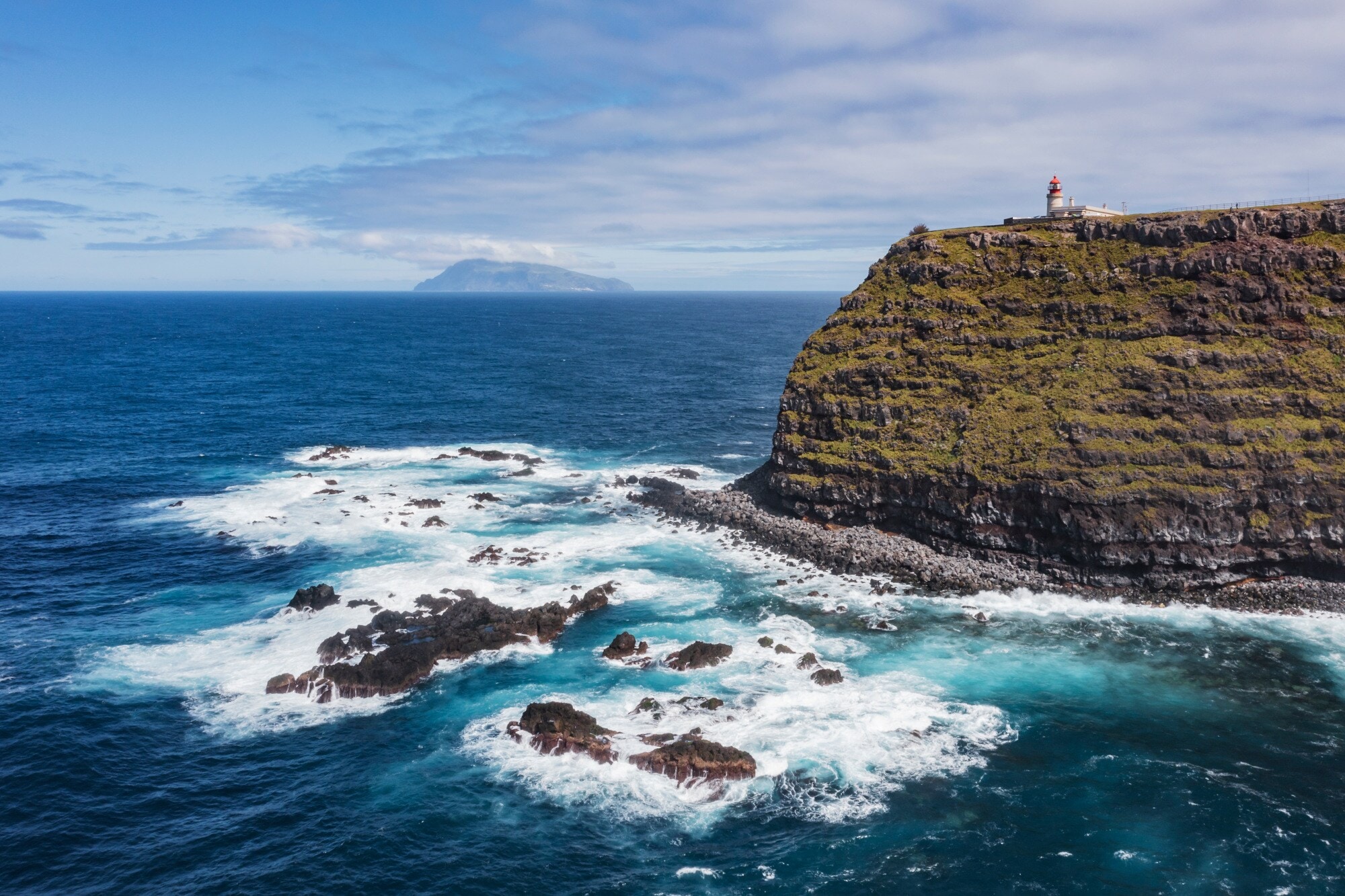 Luftaufnahme einer Steilklippe mit Leuchtturm und der Küste vorgelagerte Felsen im Meer, im Hintergrund eine Insel Luftaufnahme einer Steilklippe mit Leuchtturm und der Küste vorgelagerte Felsen im Meer, im Hintergrund eine Insel