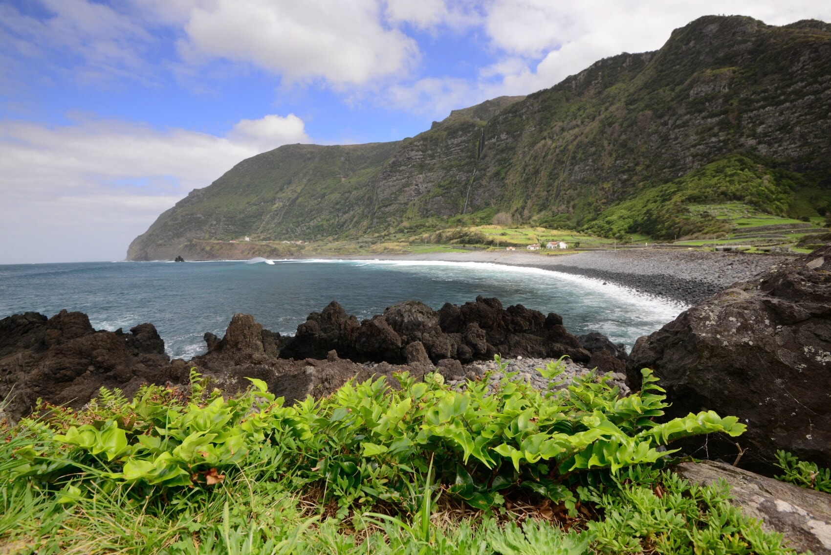 Blick auf einen Strand und dunkle Felsen mit grün bewachsenen Bergen im Hintergrund Blick auf einen Strand und dunkle Felsen mit grün bewachsenen Bergen im Hintergrund