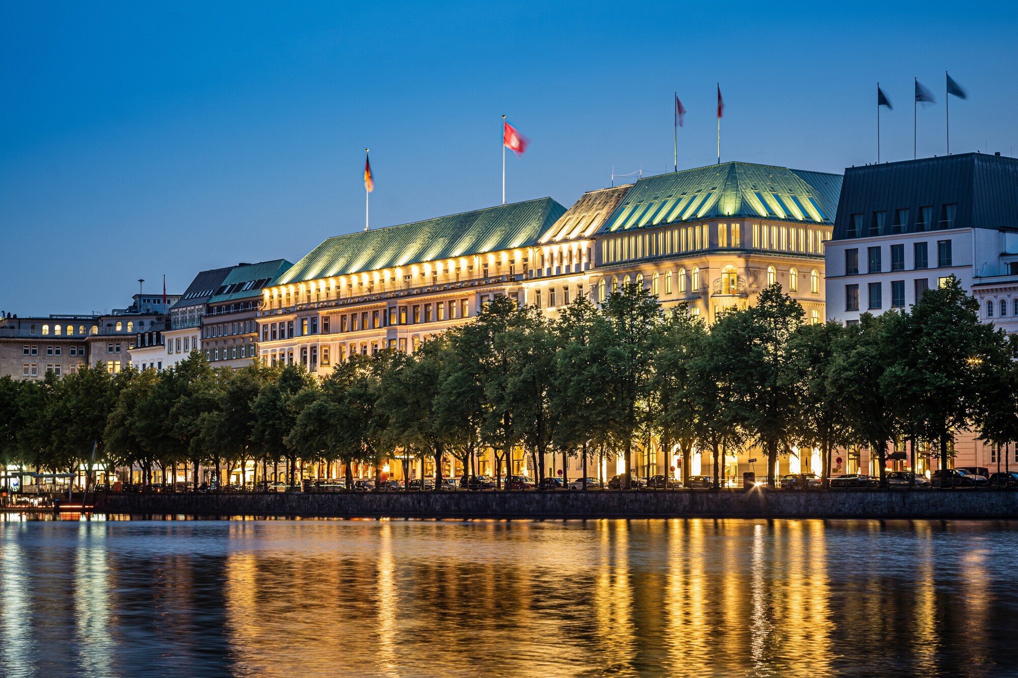 Beleuchtete Außenfassade des Hotels Vier Jahreszeiten am Wasser in der Dunkelheit.