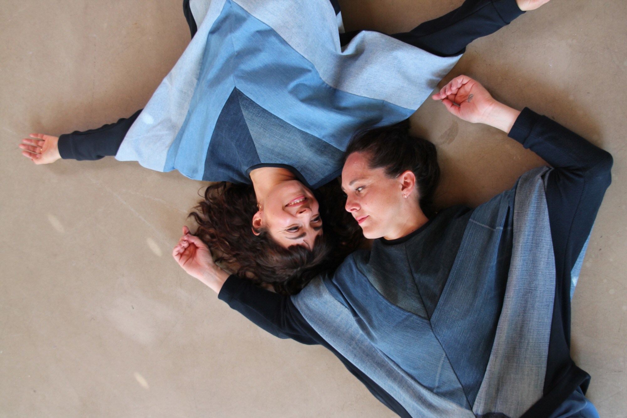 Aufsicht von zwei Frauen, die in blau gemusterten Sweatshirts kopfüber nebeneinander liegen Aufsicht von zwei Frauen, die in blau gemusterten Sweatshirts kopfüber nebeneinander liegen