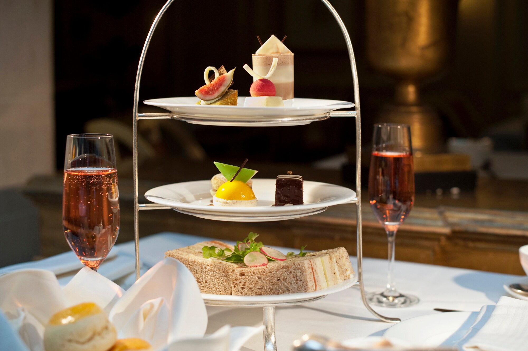 Eine Etagere mit süßen und herzhaften Häppchen auf einem edel gedeckten Tisch neben zwei Champagnergläsern