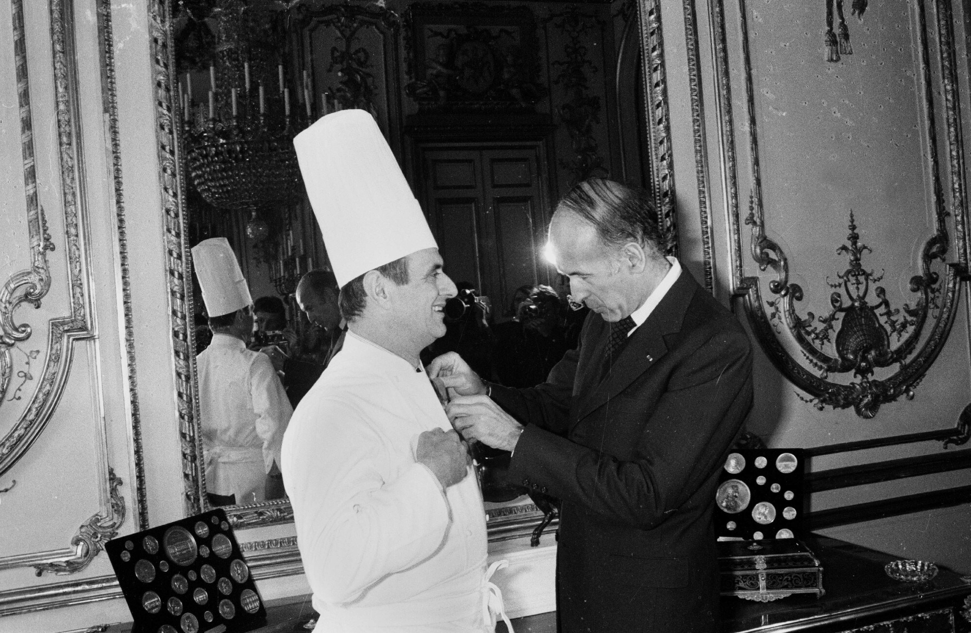 Koch Paul Bocuse bekommt im Beisein von Journalisten einen Orden von Valéry Giscard d’Estaing angesteckt, Schwarzweißaufnahme Koch Paul Bocuse bekommt im Beisein von Journalisten einen Orden von Valéry Giscard d’Estaing angesteckt, Schwarzweißaufnahme