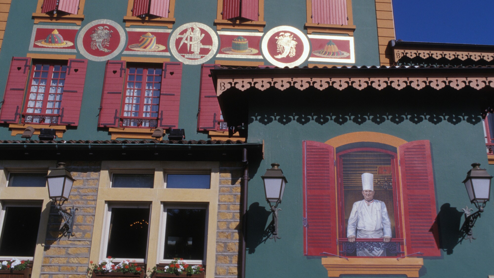Wandgemälde mit einem Porträt von Koch Paul Bocuse an der Fassade eines Restaurants mit bunten Ornamenten Wandgemälde mit einem Porträt von Koch Paul Bocuse an der Fassade eines Restaurants mit bunten Ornamenten