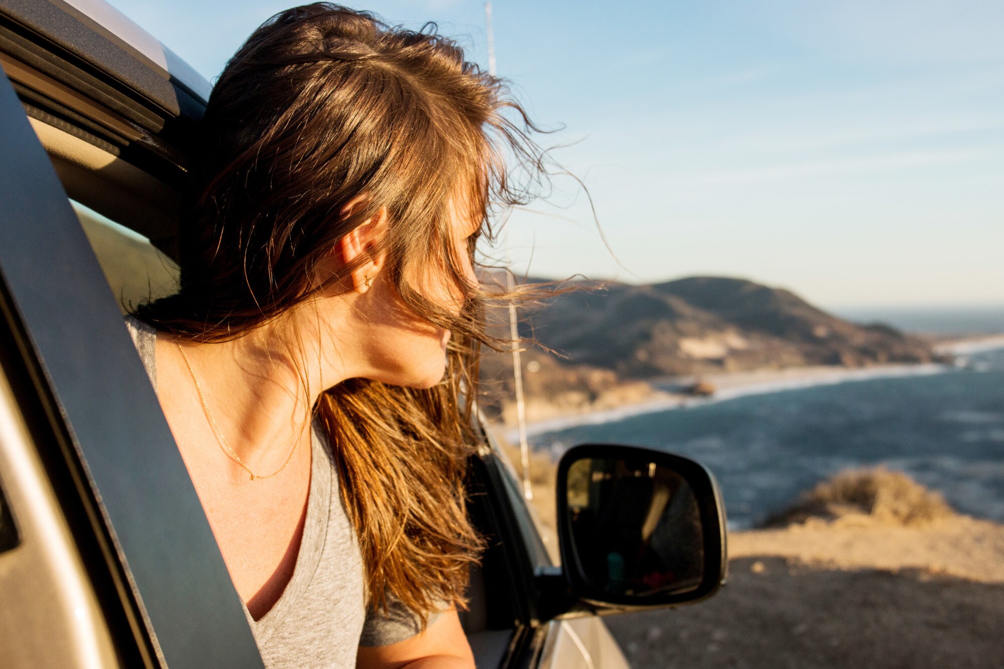 Profil einer Frau, die aus einem Autofenster auf ein Küstenpanorama schaut