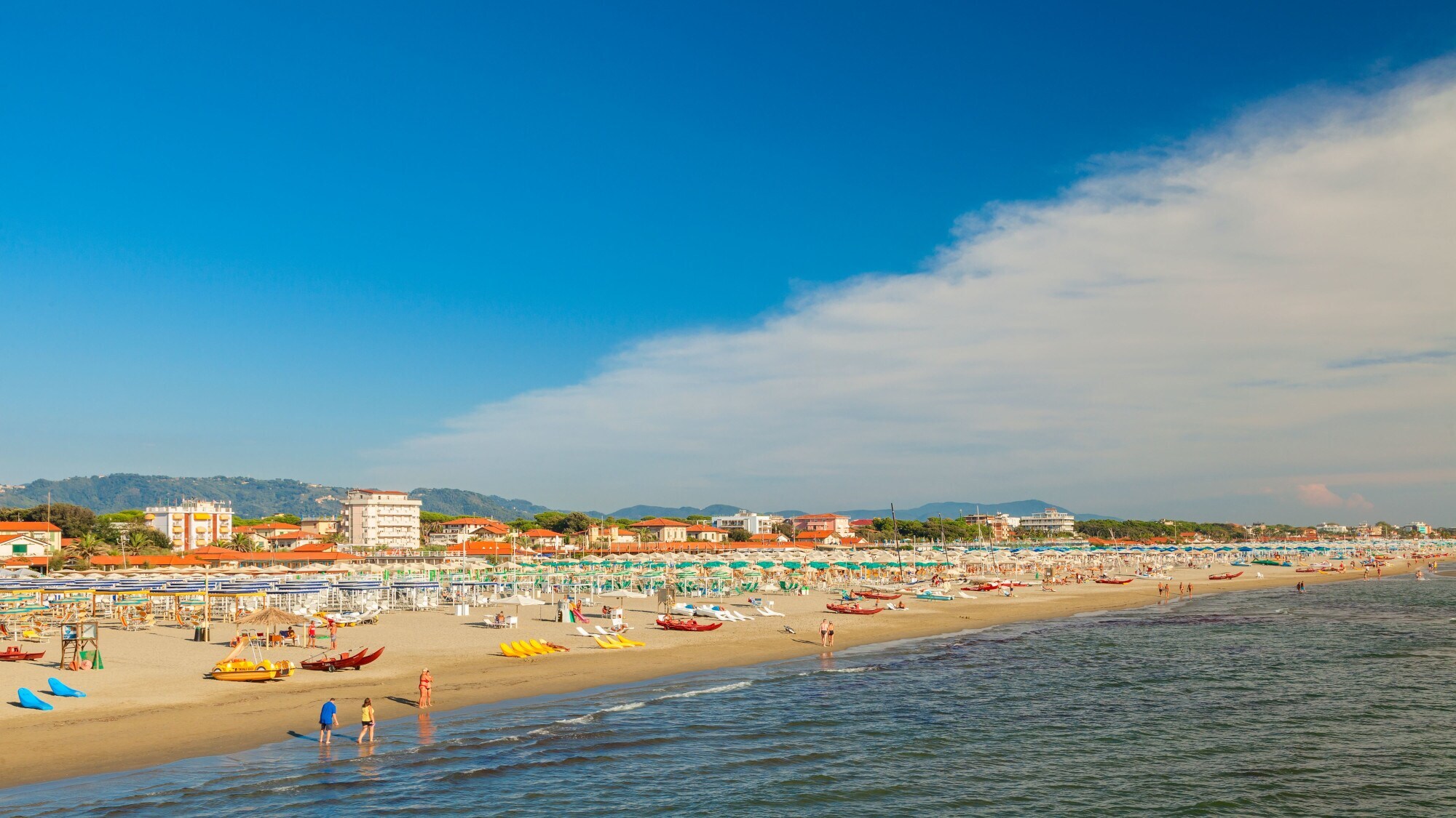 Strand mit Liegen und Sonnenschirmen, im Vordergrund das Meer