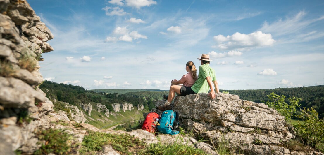 Zwei Wandernde sitzen auf einem Felsen im Altmühltal und blicken auf die Felsformation Zwölf Apostel