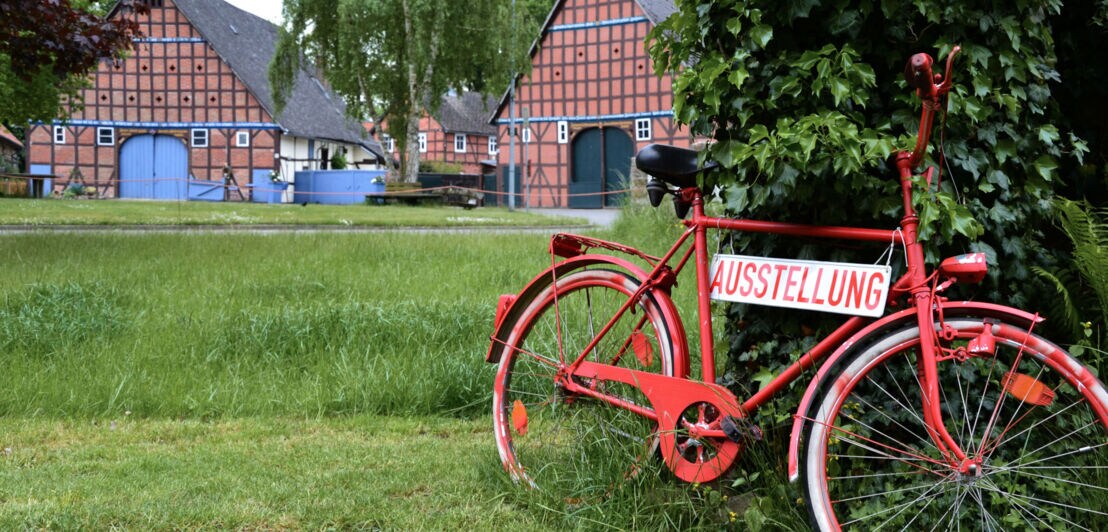 Ein an einen Baum gelehntes, rotes Fahrrad weist zu einer Ausstellung im Wendland