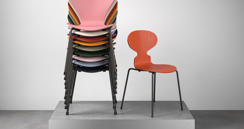 Gestapelte Stühle in vielen Farben auf einem Podest daneben ein einzelner Stuhl in rot