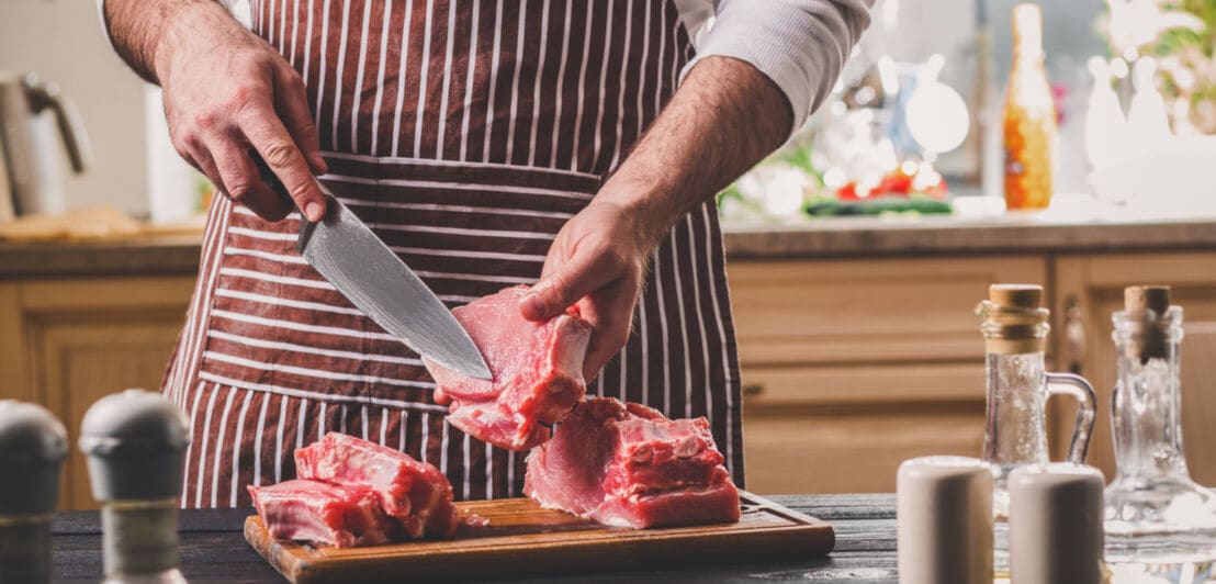 Koch schneidet Fleisch mit Messer auf Holzbrett