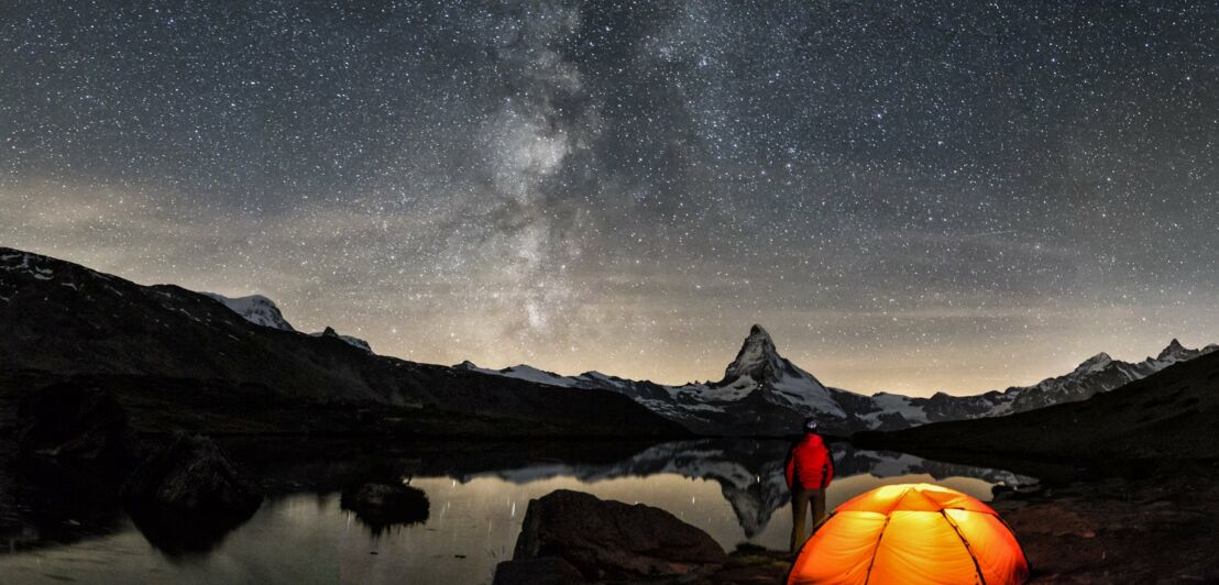 Sternenhimmel über dem Matterhorn, im Vordergrund leuchtet in der kargen Landschaft ein beleuchtetes Zelt