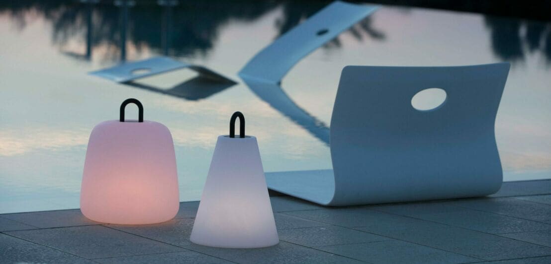Zwei portable Leuchten stehen vor einem Pool im Freien.