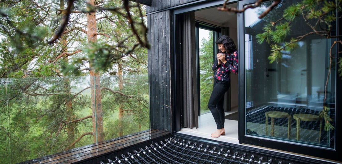 Frau steht an offener Glastür eines Baumhaushotels