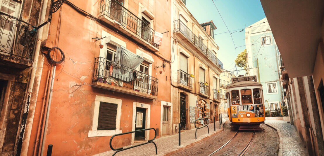 Eine Straßenbahn fährt durch eine ruhige Straße mit alten Häusern in Lissabon