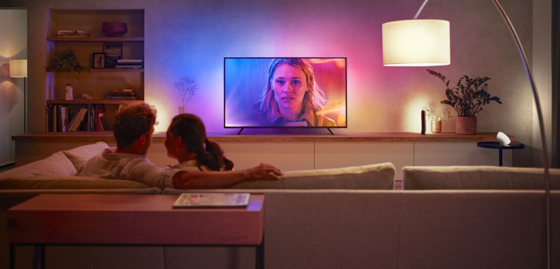 Ein Paar auf der Couch das auf einen Fernseher mit leuchtenden Farben schaut
