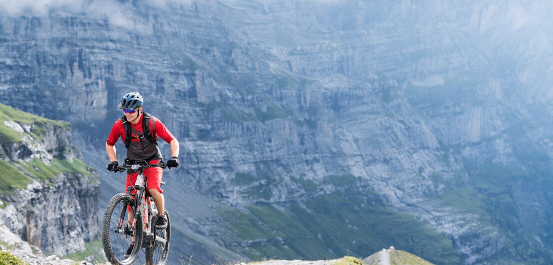 Ein Mountainbiker in rotem Dress vor einer mächtigen Felswand
