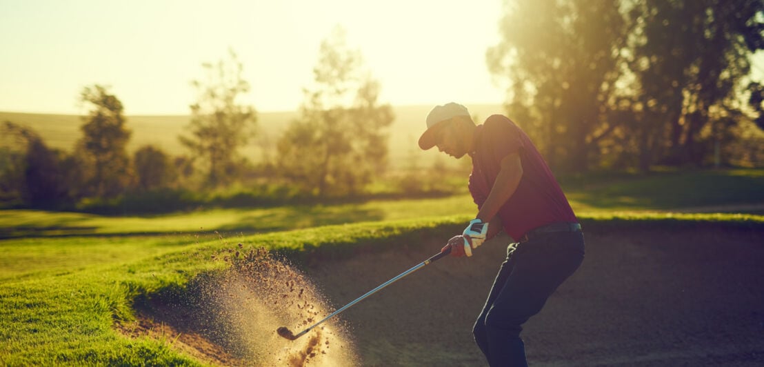 Mann schlägt Golfball aus einer Sandgrube