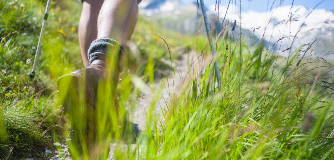 Die Beine eines Wandernden auf einem Pfad in alpinem Gelände