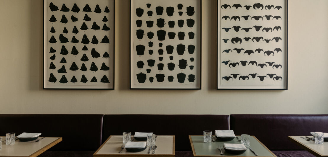 Tische eines Restaurants mit drei großen und gerahmten schwarz-weiß Drucken an der Wand