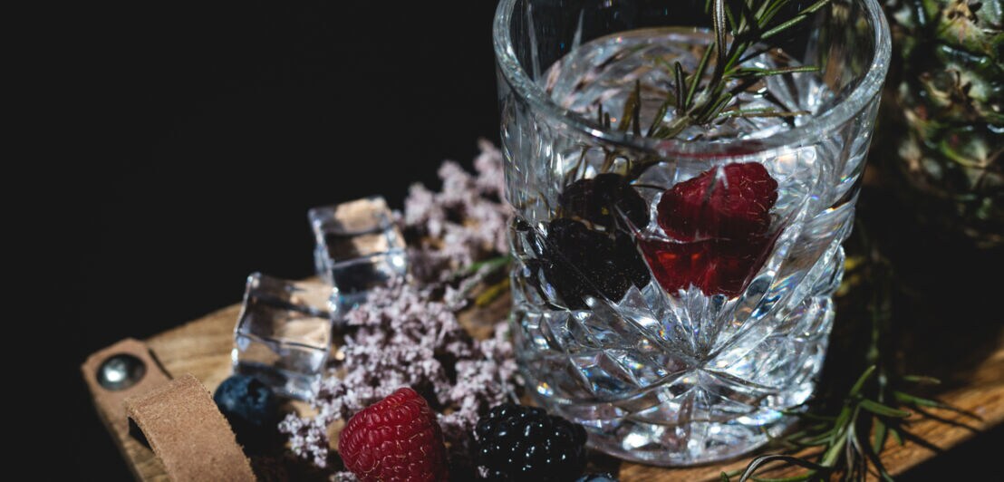 Ein geschliffenes Glas mit Gin, Beeren und Rosmarin