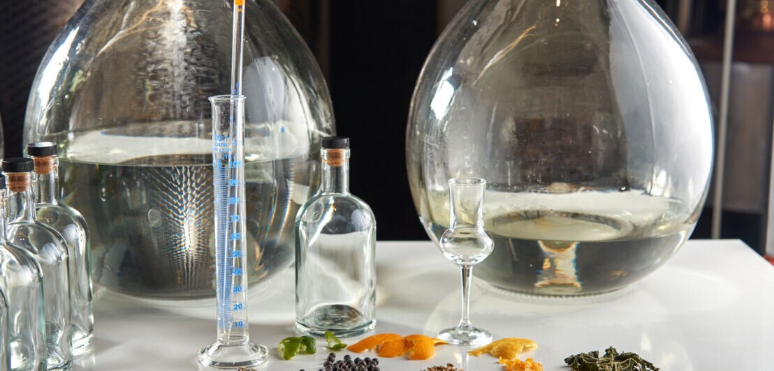 Destillierzubehör: Alkohol in großen Glasbehältern, Botanicals, Flaschen, Pipette