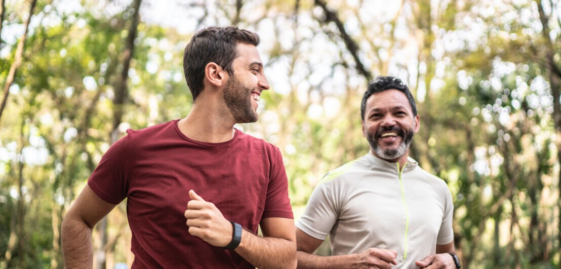 Zwei joggende, lachende Männer mit Smartwatches