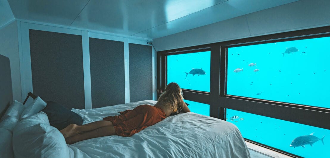 Eine Frau liegt auf ihrem Bett und beobachtet Fische